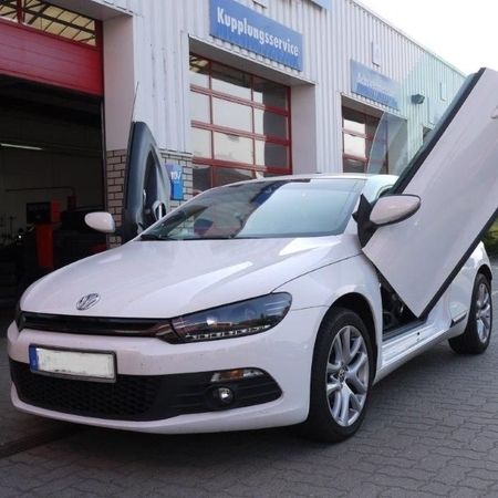 Ein weißer VW mit offenen Flügeltüren vor der Werkstatt