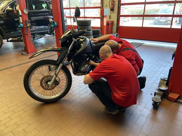 Zwei Mitarbeiter in roter Arbeitskleidung reparieren ein schwarzes Motorrad