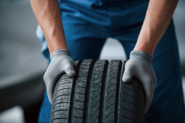 Ein Mann mit grauen Handschuhen rollt einen Autoreifen